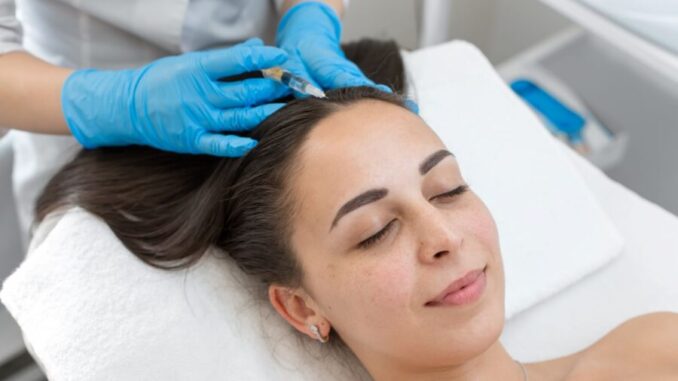 Eine Frau liegt auf einer Behandlungsliege, während eine medizinische Fachkraft mit Handschuhen eine Injektion in die Kopfhaut setzt